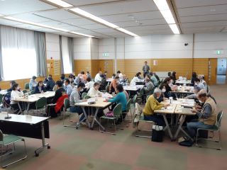 ボランティア連絡会のグループワークの様子。全体の写真。席を向かい合わせにして１グループ3～5人で話をしている。