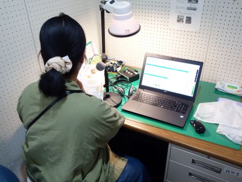 体験会参加者の録音体験の様子の写真。パソコンとマイクを前に、女性が広報を読み上げている。