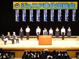 各校のジュニア奉仕団団長が活動計画発表を行っている様子の写真。壇上に一列に並んで、ひとりずつ前に出てハキハキと話している。