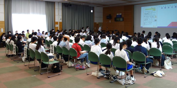 事前説明会の全体会の様子の写真。ふれあいセンター大会議室に、生徒90人弱と施設担当者20人が椅子に座って話を聞いている。