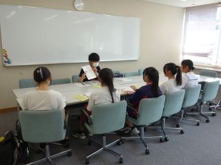 分科会の様子の写真。女子学生5人が施設担当者と向かい合わせに座って説明を受けている。