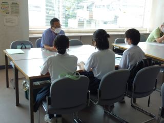 分科会の様子の写真。男女の学生3人が施設担当者と向かい合わせに座って説明を受けている。