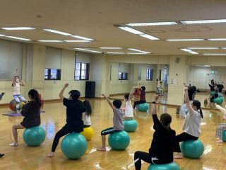 親子イベントの様子の写真。スポーツスタジオの中で親子がバランスボールに座って体操をしている。