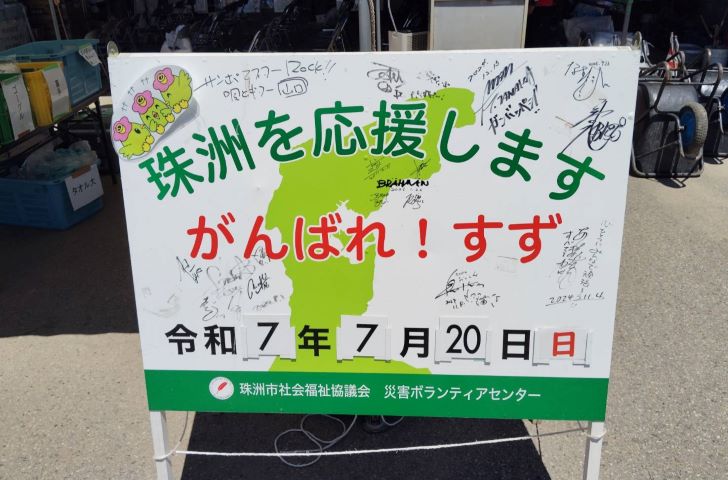珠洲市災害ボランティアセンターにある看板の写真。「珠洲を応援します　がんばれ！すず　令和7年7月20日(日)」と書かれている。文字の周りには有名人のサインが複数書いてある。