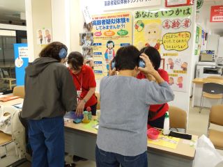 昨年度開催時の写真。高齢者疑似体験で、ヘットフォンを装着して、耳の聞こえにくさを体験している。