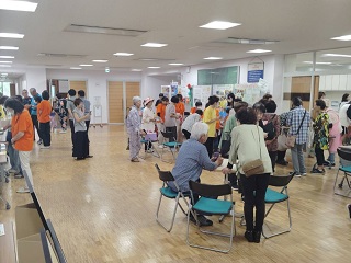 小牧西部地区つどいの写真。会場のロビーでは多くの人が各ブースで体験をしたり展示を見たりしている。