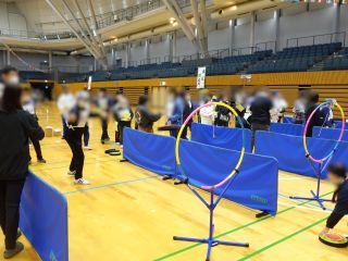 アキュラシーの写真。1.7メートルくらいの輪を地上1メートルくらいの高さにして参加者が3メートルくらい離れたところからドッチビーディスクを投げ入れている。