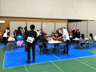 スライム企画の写真。テーブルとイスが5か所並べられ、それぞれで来場者がジュニア奉仕団の中学生から説明を受けながら思い思いのスライムを作っている。