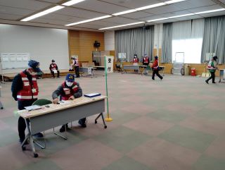 災害ボランティア支援センター演習の写真。ふれあいセンター大会議室で、受付、活動報告などのエリアに分かれてボランティアが待機している様子。