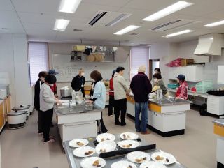 災害ボランティアの実習の写真。料理実習室で十数人で災害食を用意している様子。