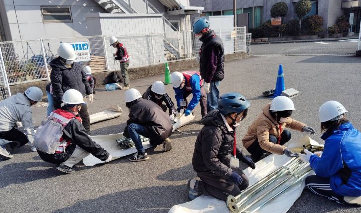 養成講座の写真。テント設営のための資材を広げて十数人が準備をしている。