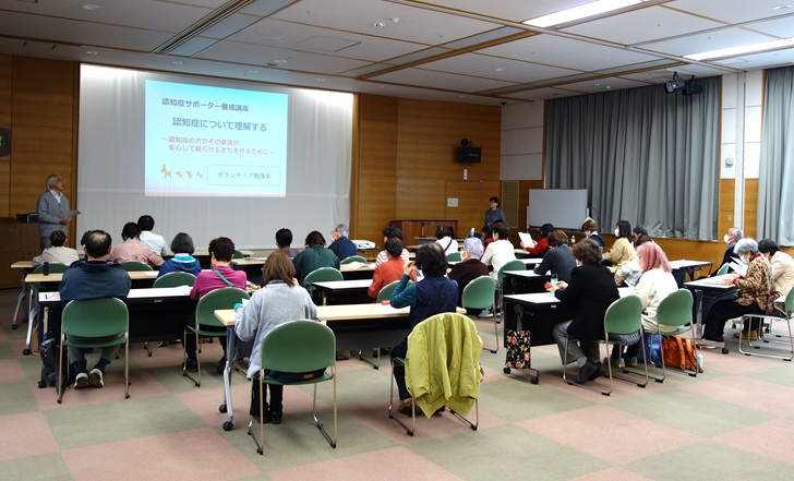 ボランティア勉強会の様子の写真。ふれあいセンター大会議室で、長机に二人掛けで、32人の参加者が椅子に座っている。皆さんの前でボランティアセンター所長が開会のあいさつをしている様子。