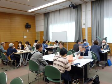 ボランティア連絡会の様子の写真。ひとグループ4人～6人でテーブルで向かい合ってテーマについて活発に話している。