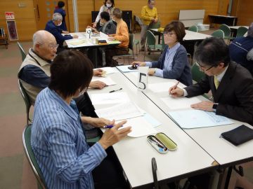 ボランティア連絡会の様子の写真。5番テーブルのグループでは、4人で自己紹介やテーマについて話したり、メモを取ったりしている。