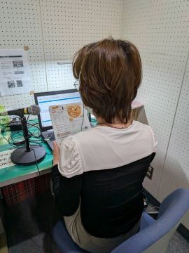 ふれあいセンター録音室に入り録音体験をしている様子。机にパソコンがあり、参加者は椅子に座って録音ソフトの入っているパソコンとマイクに向かって広報こまきの中の１ページを読んでいる。