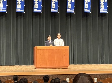 高校生ボランティア「ココボラ」の今年度の代表2名が壇上でお話をしている写真。それぞれが通っている高校の制服を着た男女。