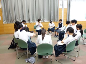 事前説明会の写真。分科会の様子。全体会のあった大会議室の一画で、施設担当者1名と生徒12名が輪になり椅子に座っている。