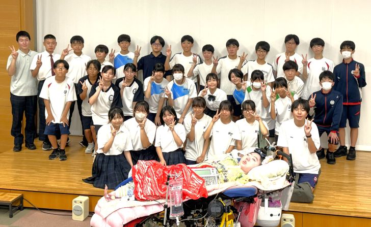 歌子さんと参加した生徒32人の集合写真。手前に移動ベッドに横になっている歌子さんがいて、その後ろに3列ほどに並んで生徒たちが笑顔で写っている。