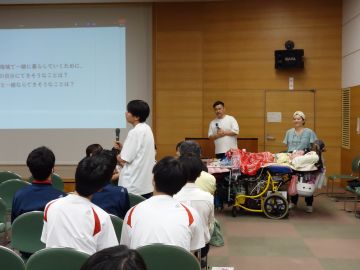 代表の生徒が起立してマイクを持ち、「自分が地域のためにできること」について発表している様子の写真。