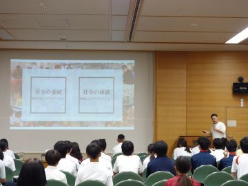 生徒たちがプロジェクターを見ながら、講師の話を聞いている様子の写真。