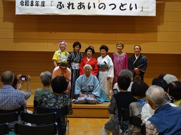 和楽桜会(わらおうかい)の写真。写真奥の舞台上に和楽桜会のメンバーが集合し記念撮影をしている。着物や、ドレスを着た男女8人が並び参加者に笑顔を向け、何人かの参加者がカメラを向け、その様子を撮影している。