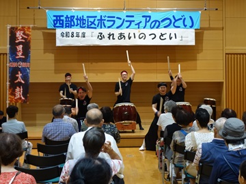 和太鼓グループの堅塁太鼓(けんるいだいこ)の写真。写真奥の舞台上に和太鼓が並び、5人の男性が力強く太鼓を叩いている。