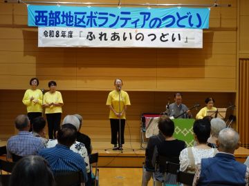 森民謡会(もりみんようかい)の写真。舞台上に5人おり、左には手拍子をしている女性2人、正面で歌っている女性1人、右には座って三味線を演奏している男女2人。