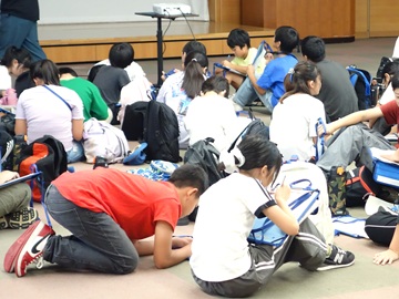 大会議室に戻ってきた子どもたちが床に座りそれぞれ用紙に今日の振り返りをまとめている様子。