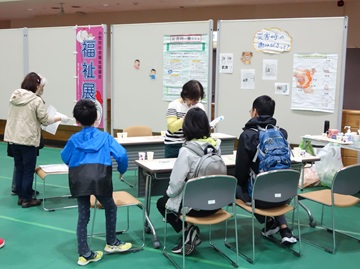 昨年の様子の写真。「こまき歯っ磨るテイスターズ」のブースでは、口腔ケアの体験ができ、来場者の家族の両親が椅子に座り体験している。
