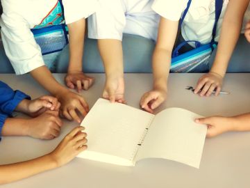 点字で書かれた見本の冊子を、何人もの子どもたちが思い思いに触っている様子。